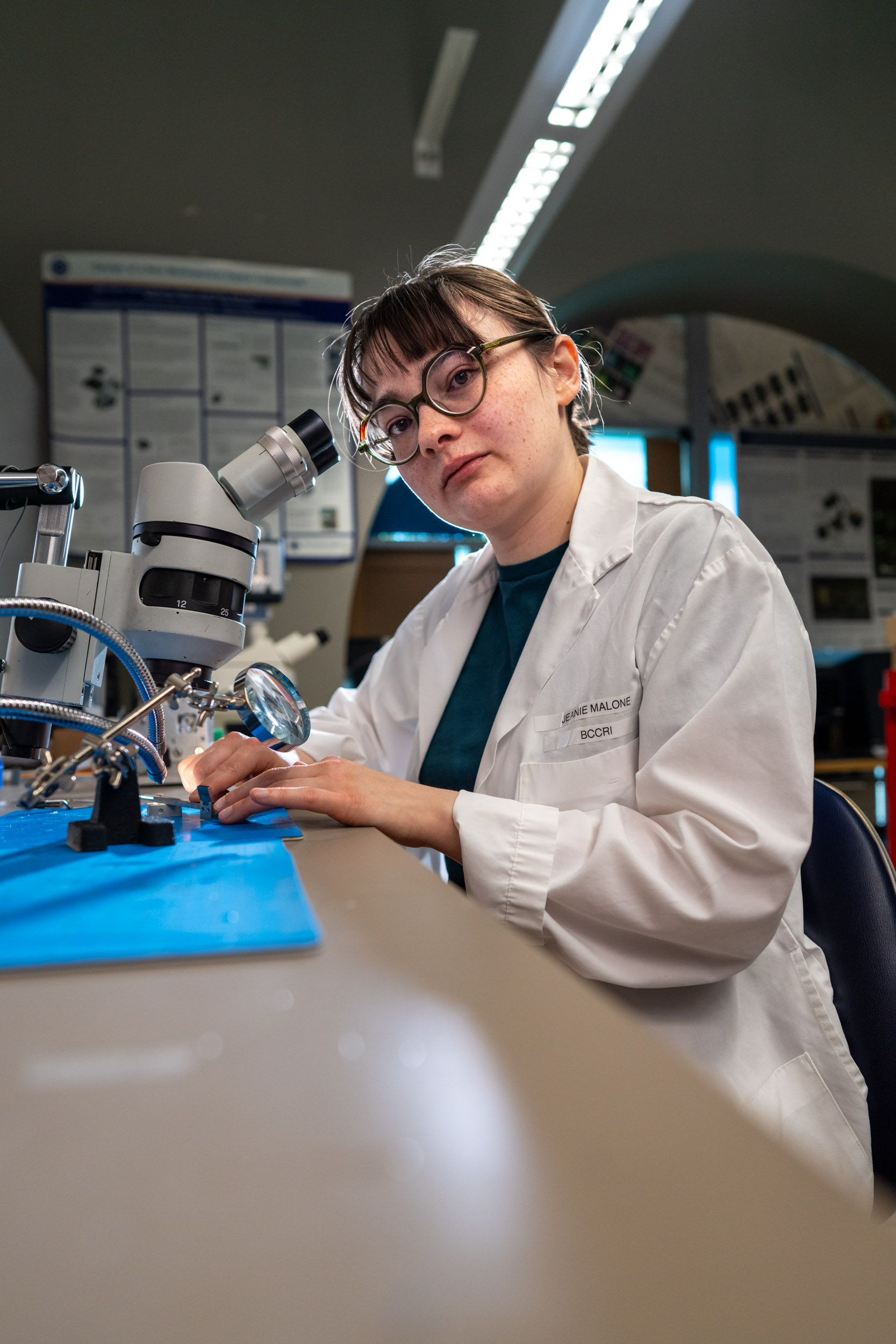 Researcher in white lab coat at microscope with confident look
